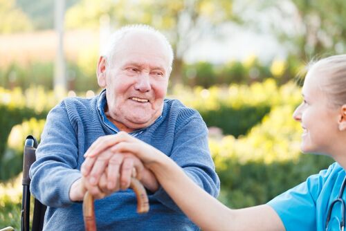 Senior in rolstoel krijgt hand van verpleger